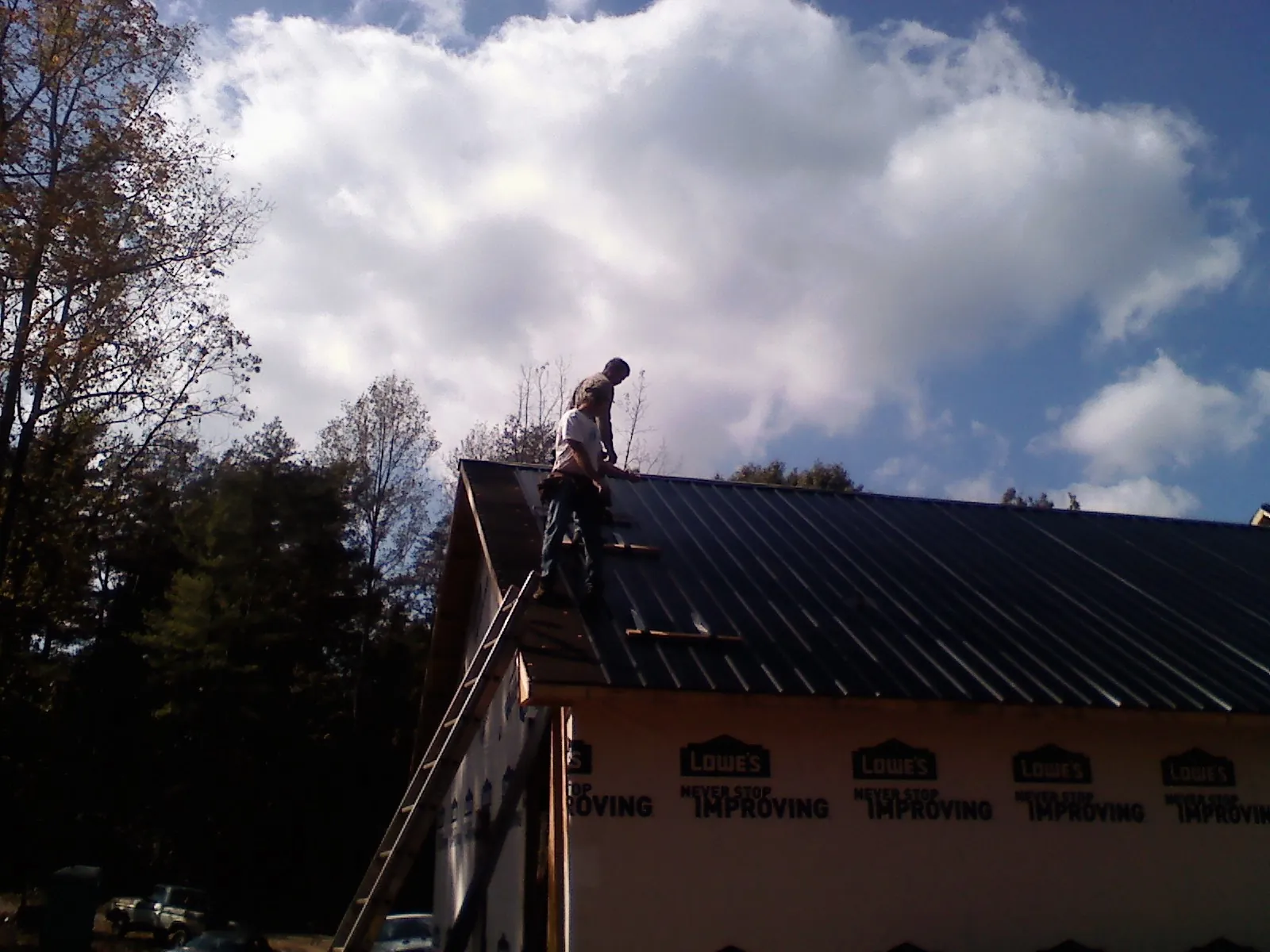 Roofer fastening dark metal panels high against a cloudy sky, from a Roof Inspection job in Ridgeway